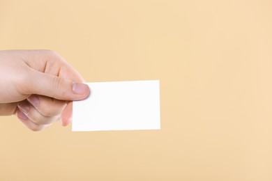 Man holding paper card on pale orange background, closeup. Mockup for design