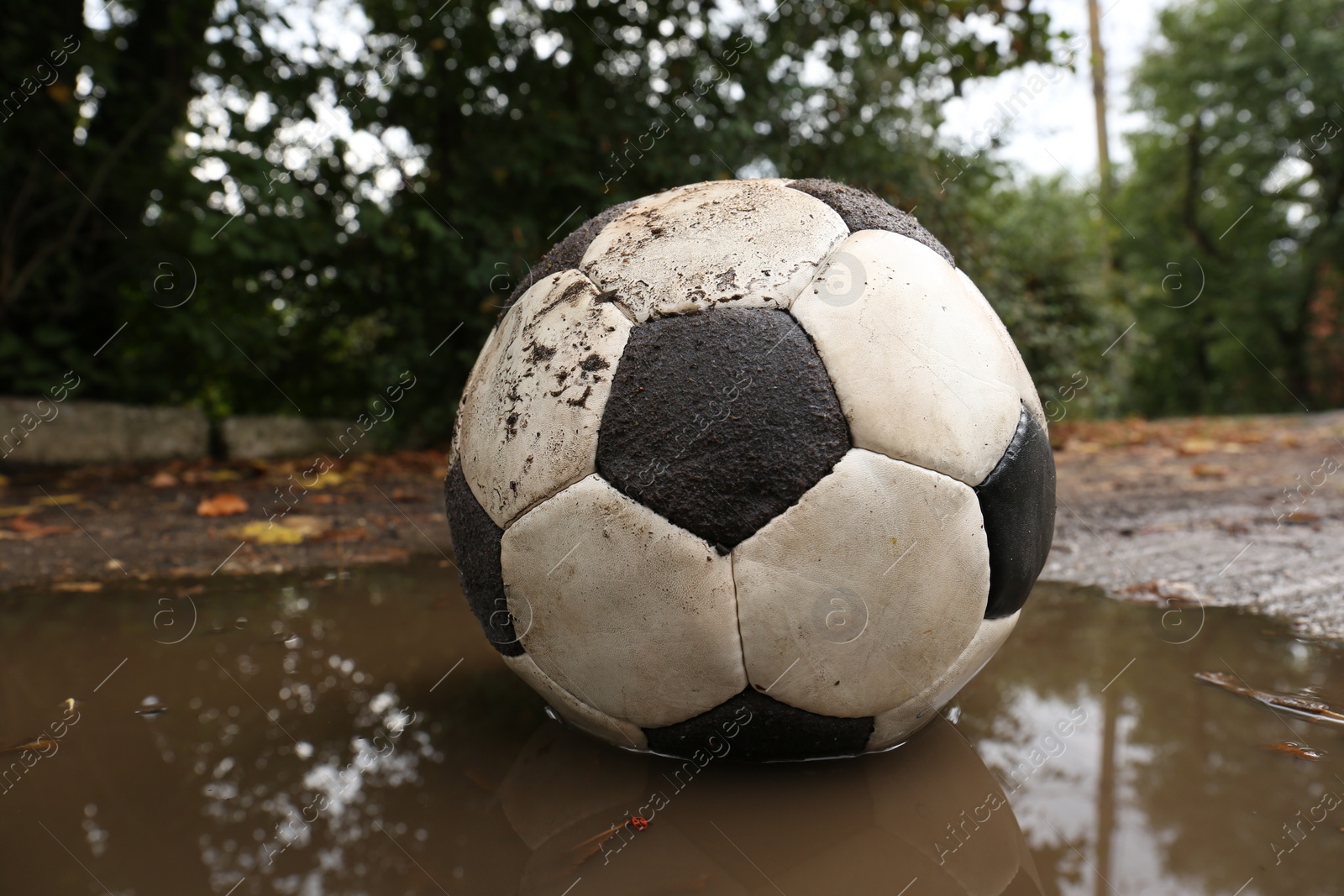 Photo of Dirty soccer ball in muddy puddle, closeup