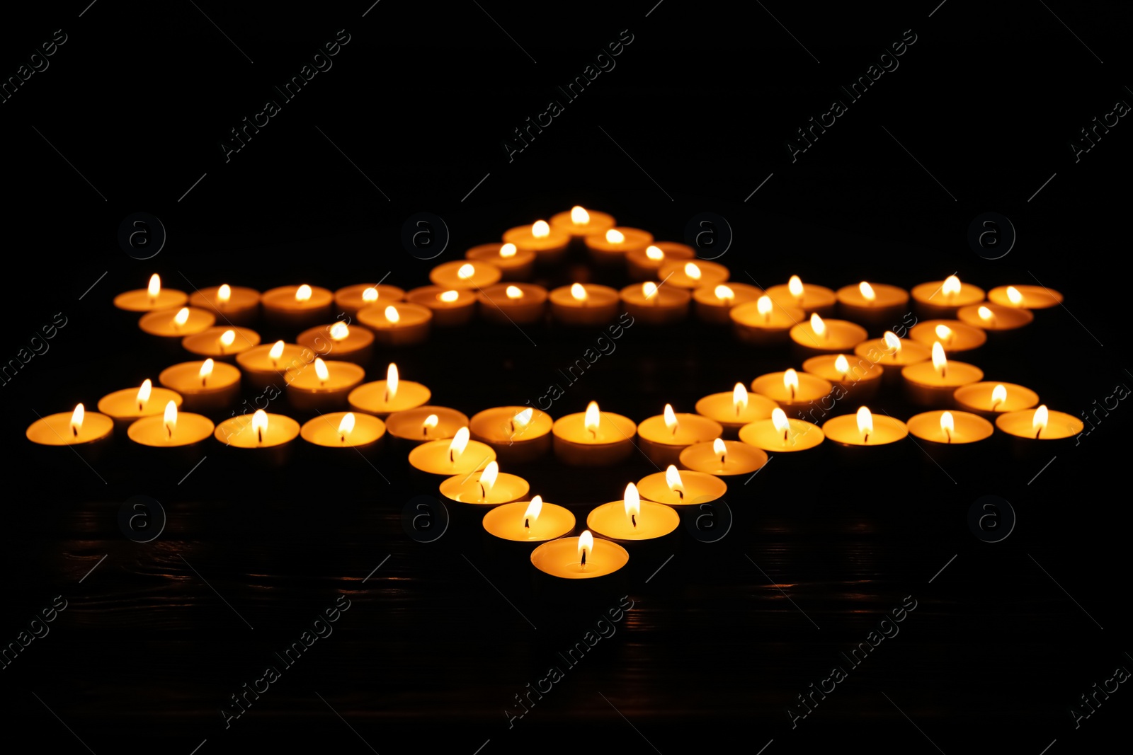 Photo of Star of David made with burning candles on black background. Memory day