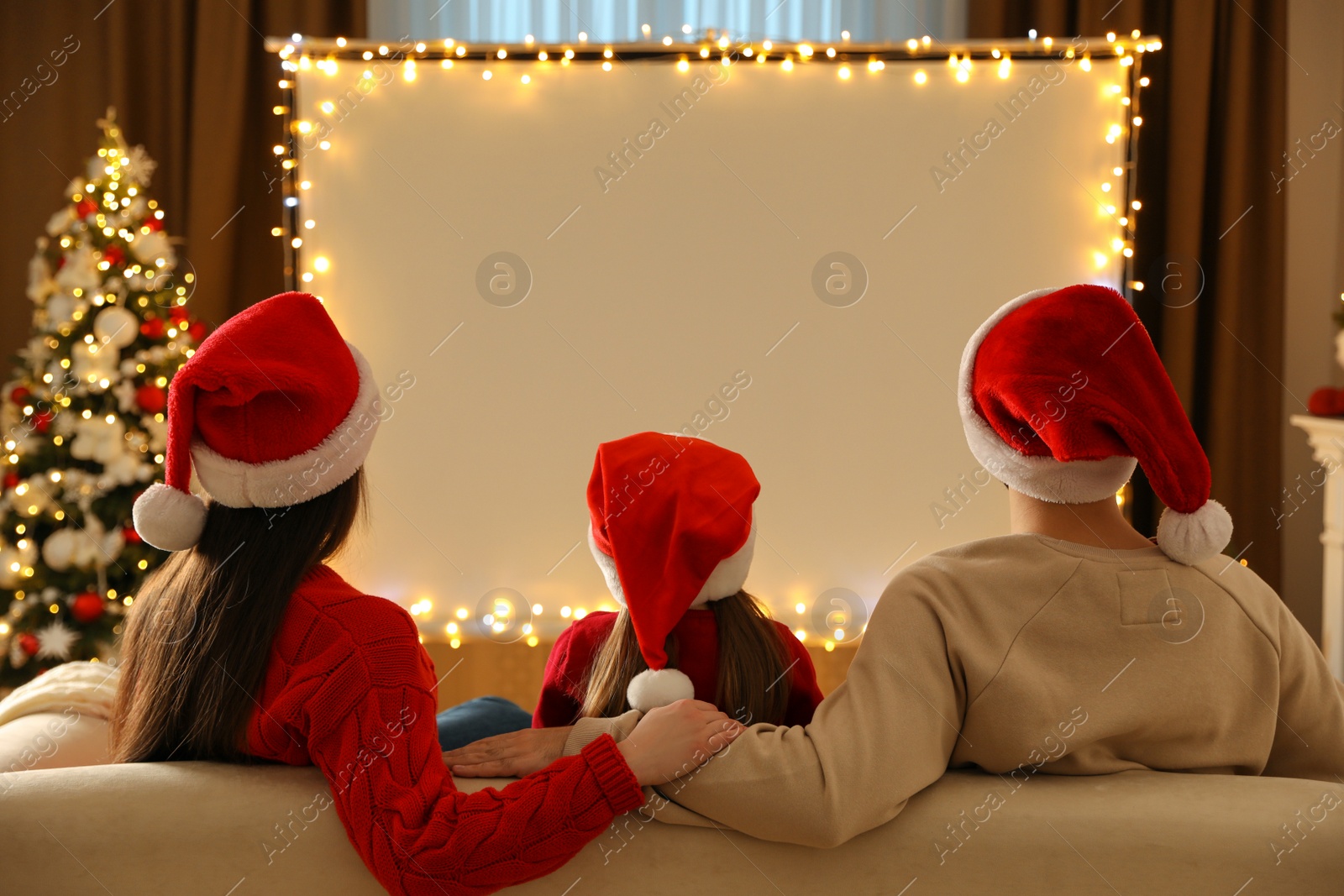 Photo of Family watching movie on projection screen in room decorated for Christmas, back view. Home TV equipment
