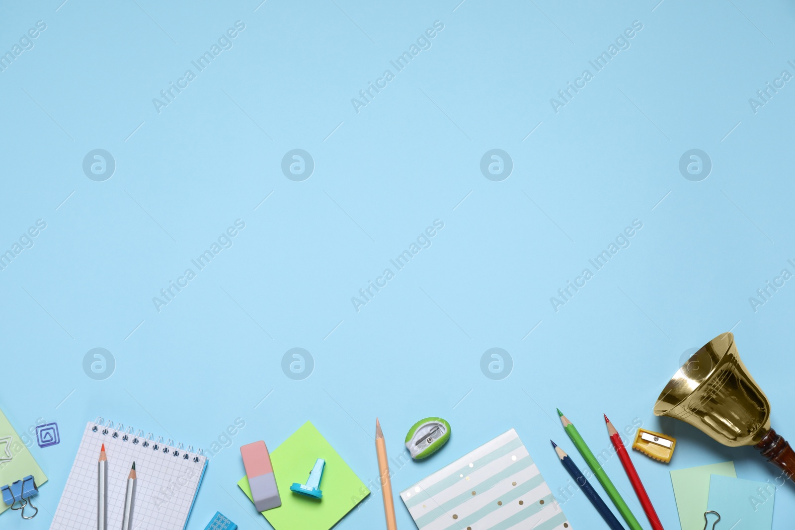 Photo of Different stationery and school bell on light blue background, flat lay. Space for text