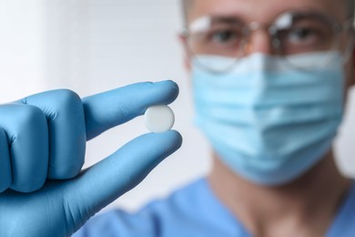 Doctor holding pill on light background, selective focus. Space for text