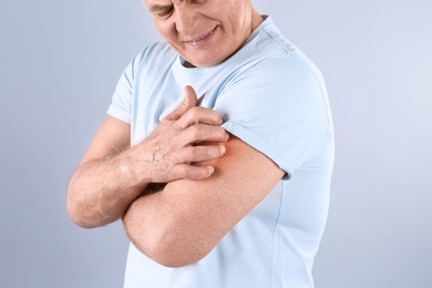 Photo of Senior man scratching arm on grey background, closeup. Allergy symptom