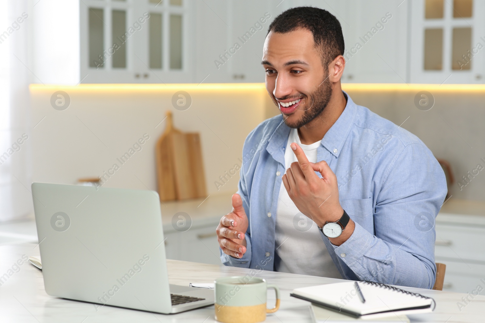 Photo of Young man having online video chat at desk in kitchen. Home office