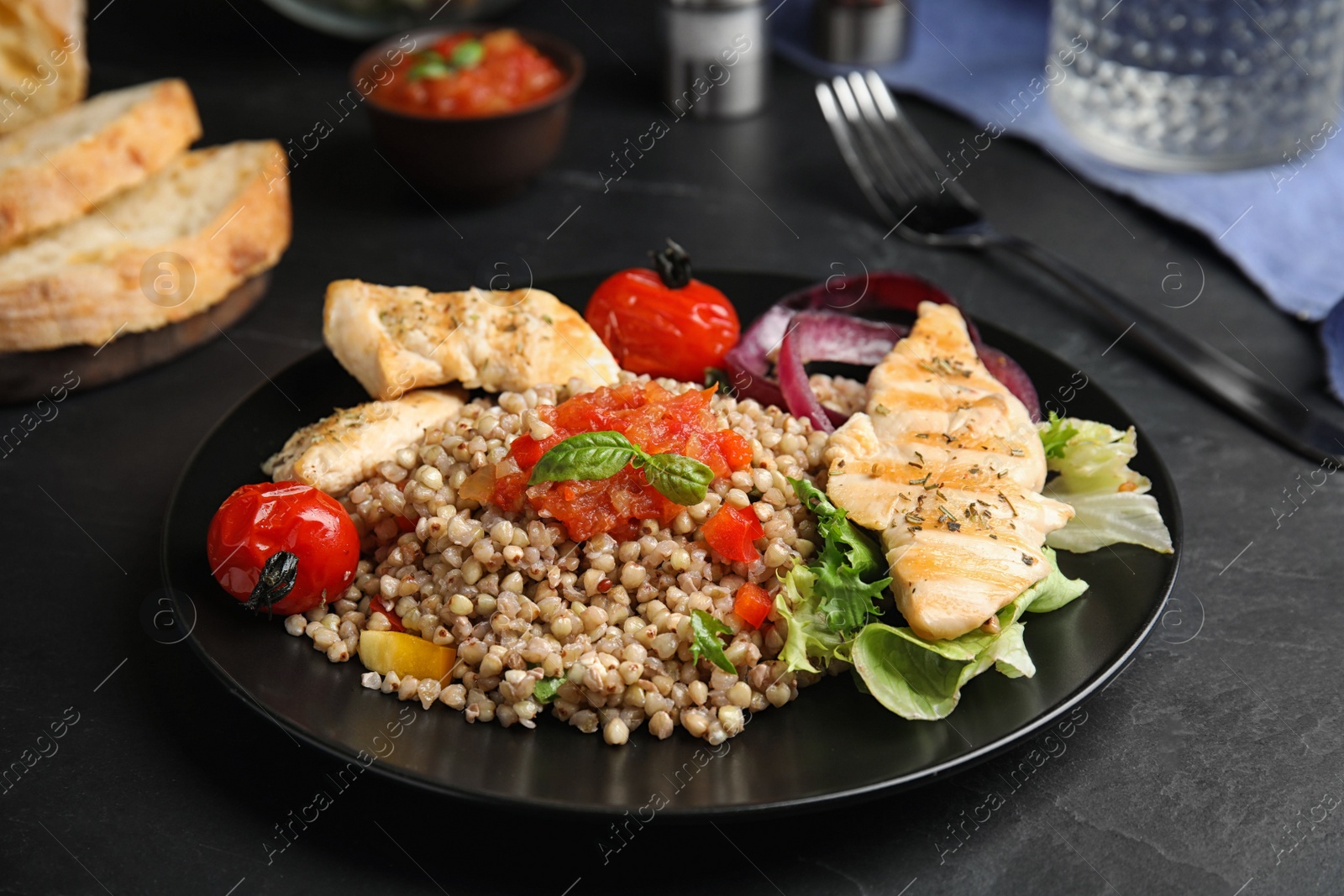 Photo of Tasty buckwheat porridge with meat and vegetables on black table