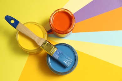 Photo of Jars of different paints and brush on color background, flat lay