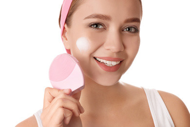 Young woman washing face with brush and cleansing foam on white background. Cosmetic products