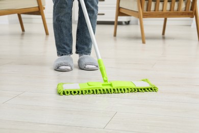 Photo of Woman cleaning dirty white parquet floor with mop indoors, closeup