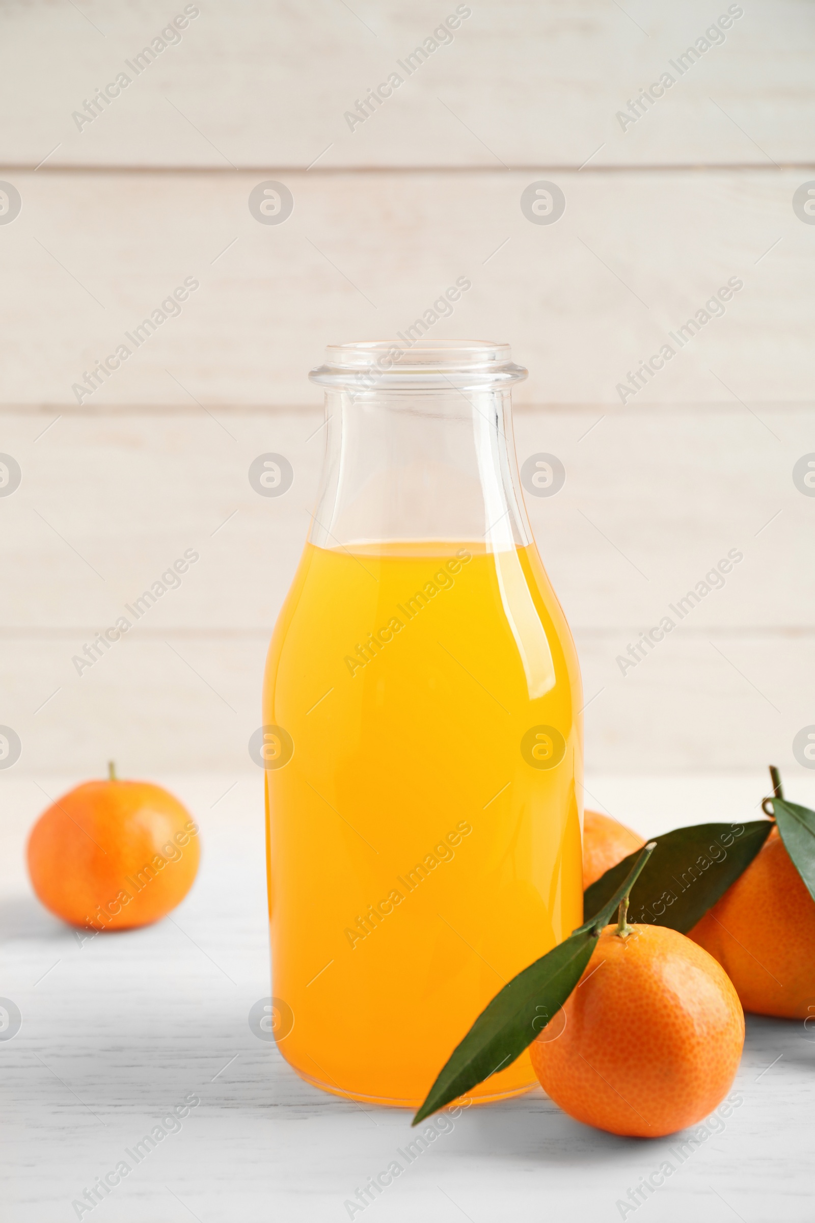 Photo of Fresh tangerines and bottle of juice on white wooden table