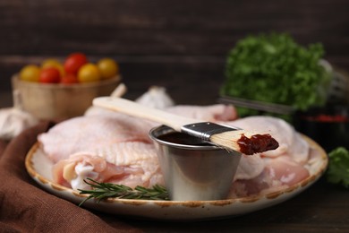 Photo of Plate with marinade, raw chicken and basting brush on table, closeup