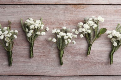 Photo of Many small stylish boutonnieres on light wooden table, flat lay