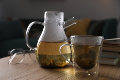 Photo of Glass teapot and cup of hot tea on wooden table in living room. Cozy home atmosphere