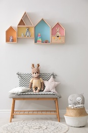 Photo of House shaped shelves and bench with toys in children's room. Interior design