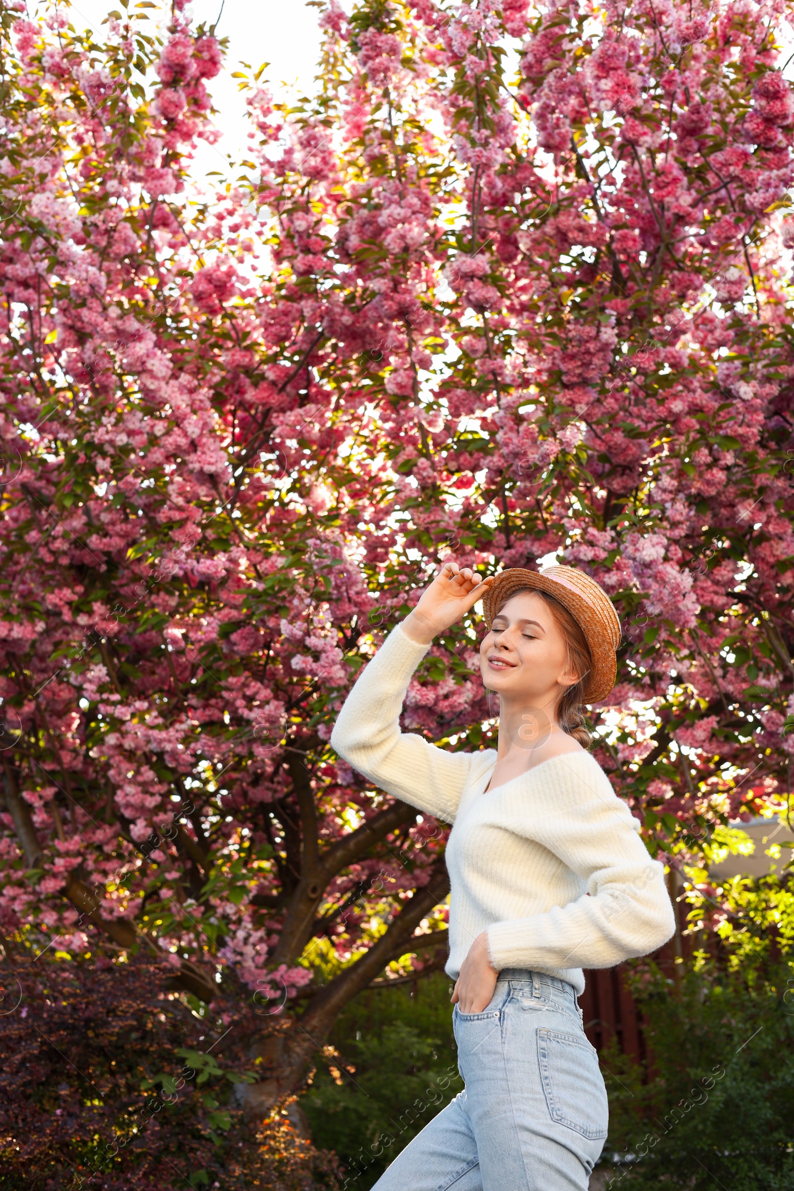 Photo of Beautiful teenage girl with hat near blossoming tree in spring