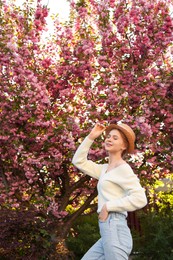 Photo of Beautiful teenage girl with hat near blossoming tree in spring