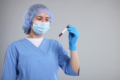 Laboratory testing. Doctor with blood sample in tube on light grey background, space for text