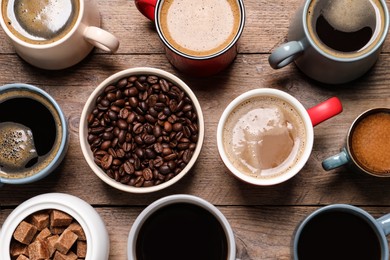 Photo of Cups of hot coffee with beans and sugar on wooden table, flat lay