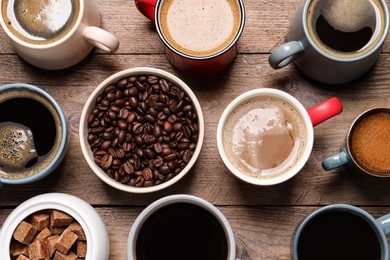 Cups of hot coffee with beans and sugar on wooden table, flat lay