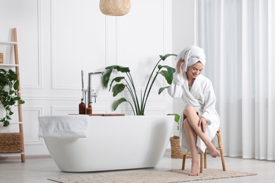 Photo of Beautiful young woman touching her smooth legs in bathroom, space for text