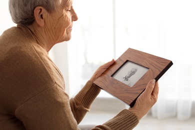 Elderly woman with framed photo of her son at home
