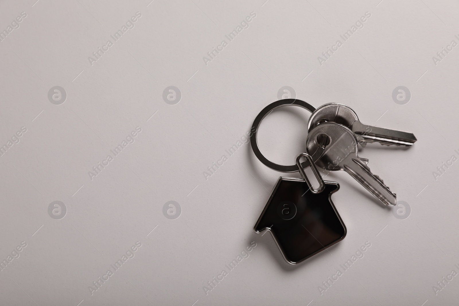 Photo of Keys with trinket in shape of house on white background, top view and space for text. Real estate agent services