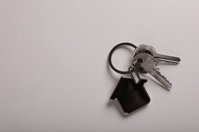 Keys with trinket in shape of house on white background, top view and space for text. Real estate agent services