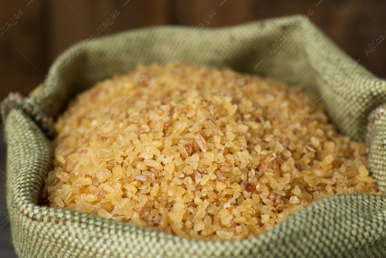 Photo of Closeup view of burlap bag with dry uncooked bulgur