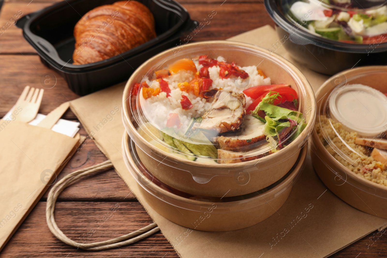 Photo of Tasty food in containers with knife and fork on wooden table, closeup