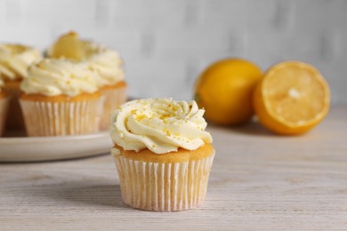 Photo of Delicious cupcakes with white cream and lemon zest on light wooden table, closeup