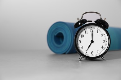 Photo of Alarm clock, yoga mat and dumbbells on grey background, space for text. Morning exercise