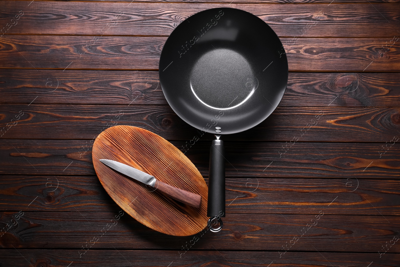 Photo of Empty iron wok, knife and cutting board on wooden table, flat lay