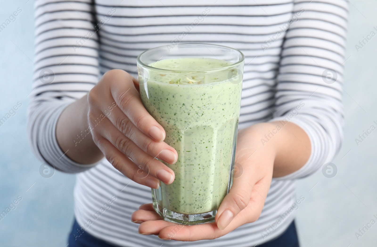 Photo of Woman holding green buckwheat smoothie on light blue background, closeup