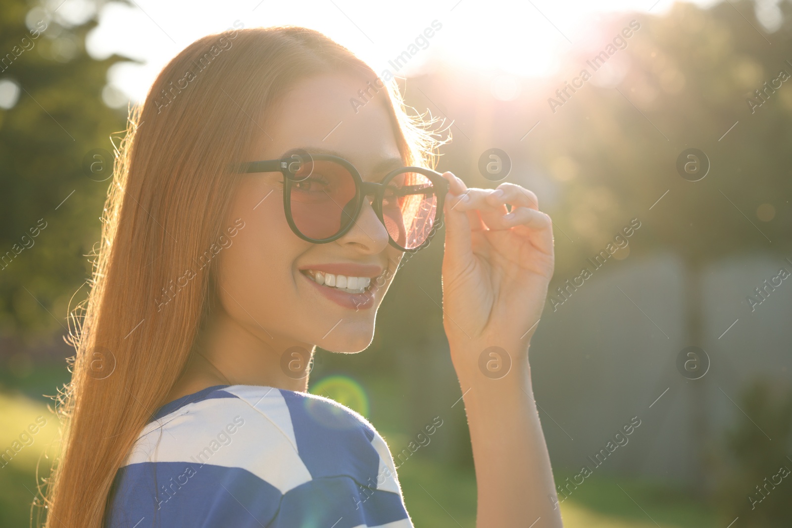 Photo of Beautiful smiling woman wearing sunglasses in park, space for text