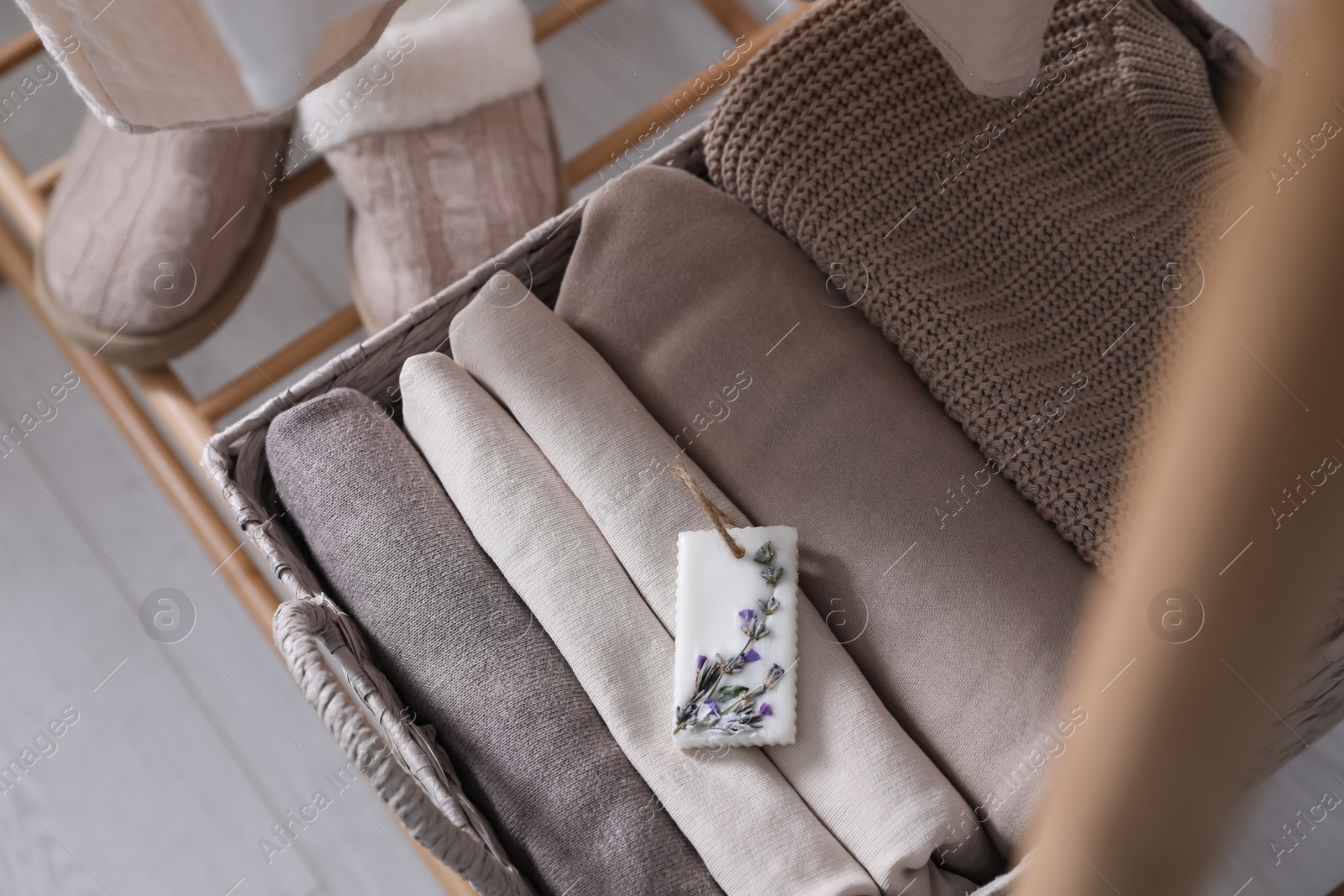 Photo of Beautiful scented wax sachet and folded clothes in wicker basket on rack, above view