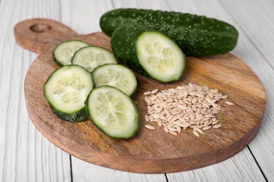 Photo of Pile of vegetable seeds and fresh cucumbers on white wooden table, closeup