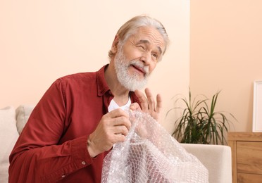 Emotional senior man popping bubble at home. Stress relief