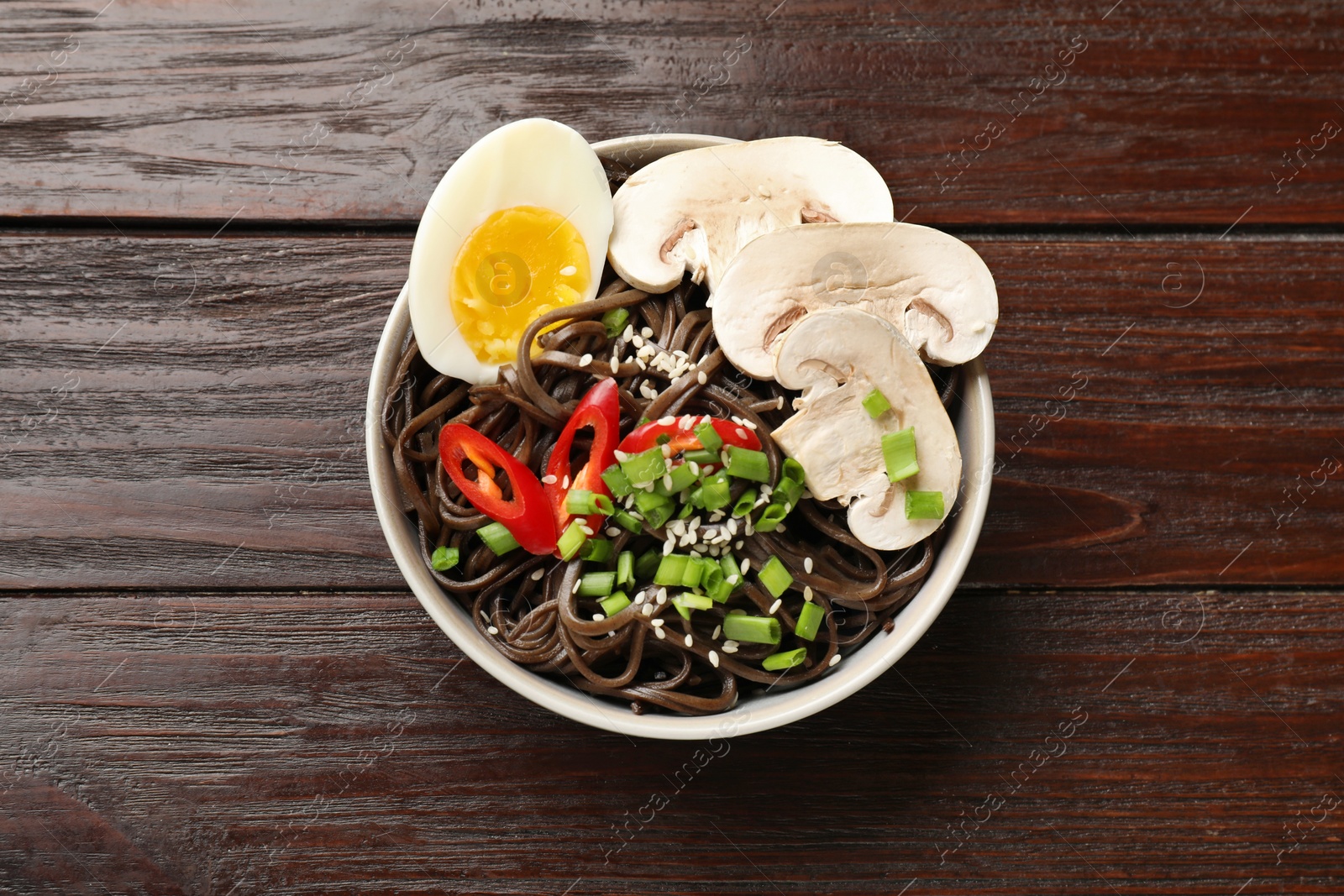 Photo of Tasty buckwheat noodles (soba) with mushrooms, egg and chili pepper in bowl on wooden table, top view