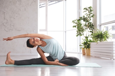 Young woman practicing revolved head to knee asana in yoga studio. Parivrtta Janu Sirsasana pose
