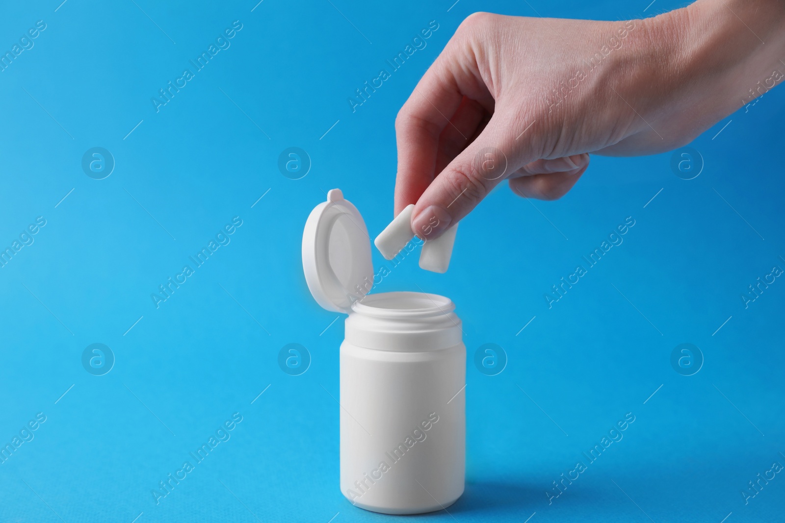 Photo of Woman taking chewing gums from jar on light blue background, closeup