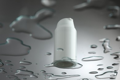 Moisturizing cream in bottle on glass with water drops against grey background, low angle view