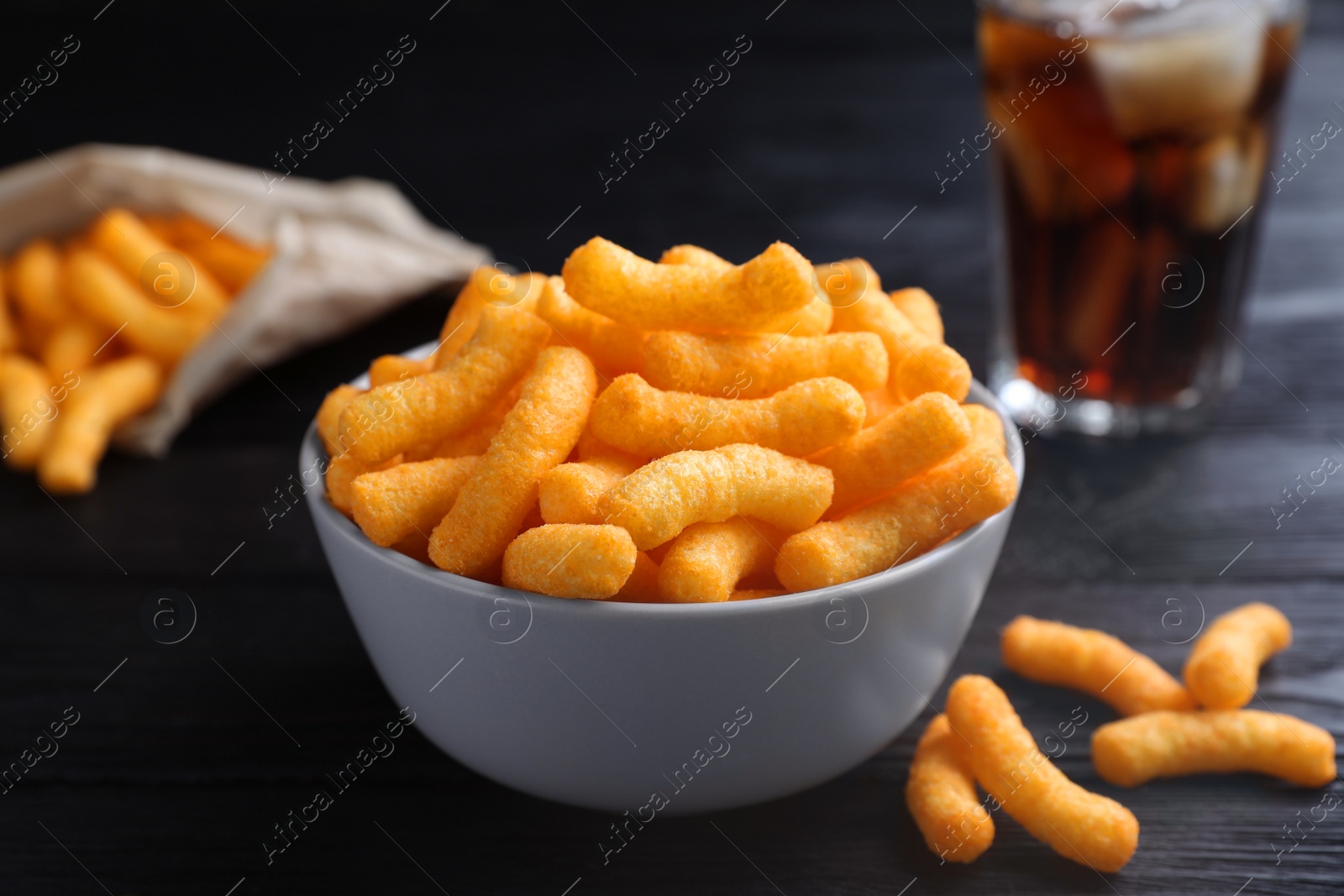 Photo of Bowl with crunchy cheesy corn snack on black wooden table, closeup