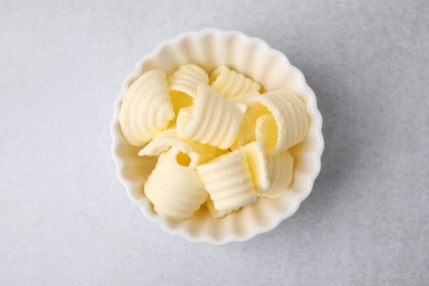Photo of Tasty butter curls in bowl on light grey table, top view
