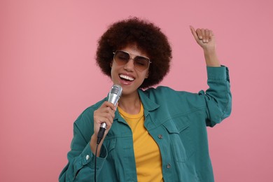 Curly young woman in sunglasses with microphone singing on pink background