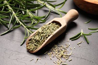 Photo of Wooden scoop with dry and fresh rosemary on black table, closeup