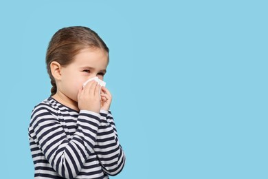 Photo of Girl blowing nose in tissue on light blue background, space for text. Cold symptoms