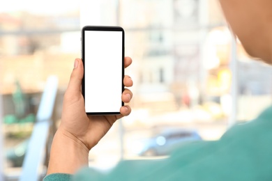 Photo of Man holding smartphone with blank screen on blurred background, closeup of hand. Space for text