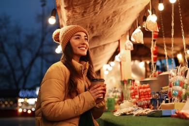 Photo of Young woman with cup of hot drink spending time at Christmas fair, space for text