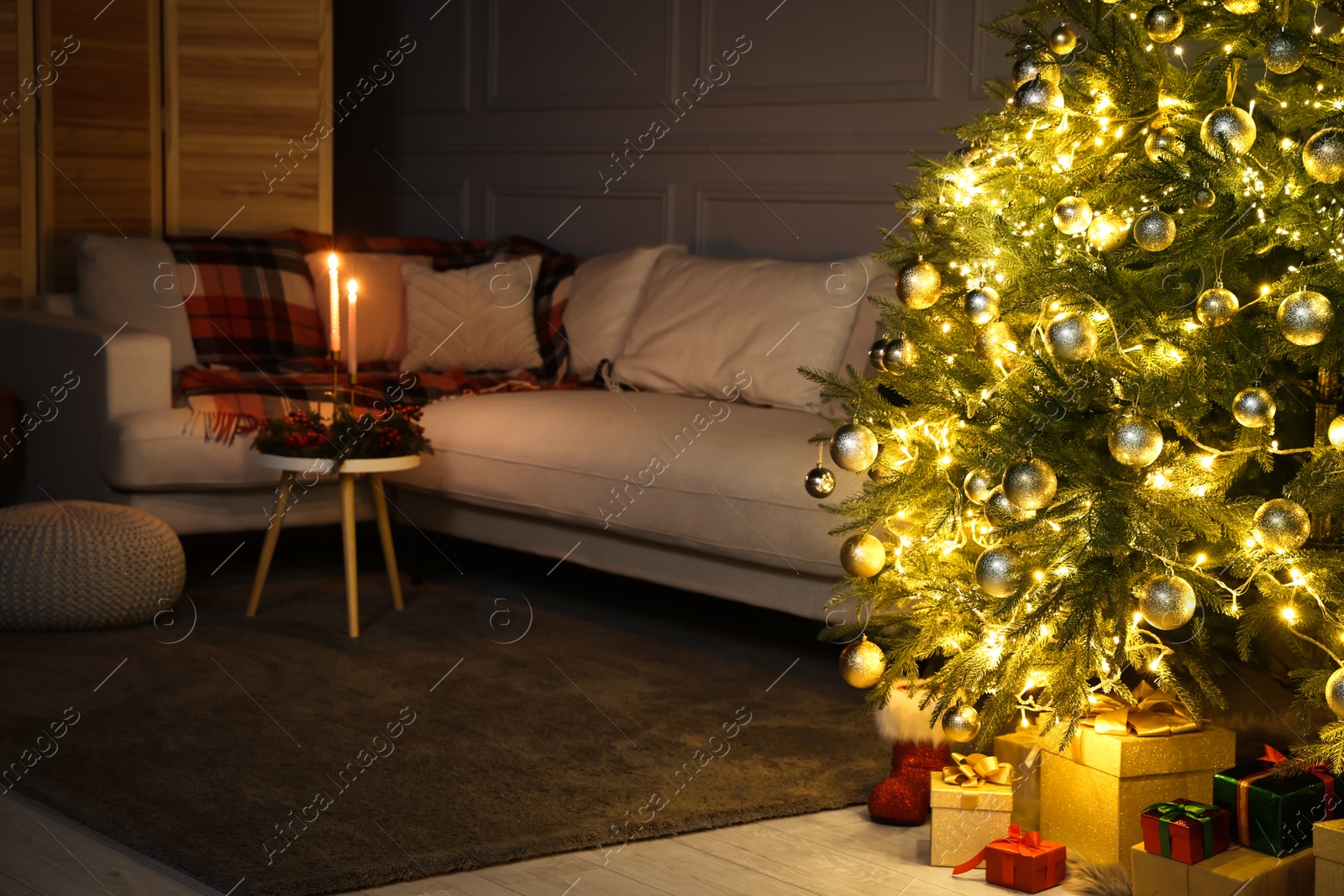 Photo of Beautiful glowing Christmas tree, gift boxes and sofa in living room