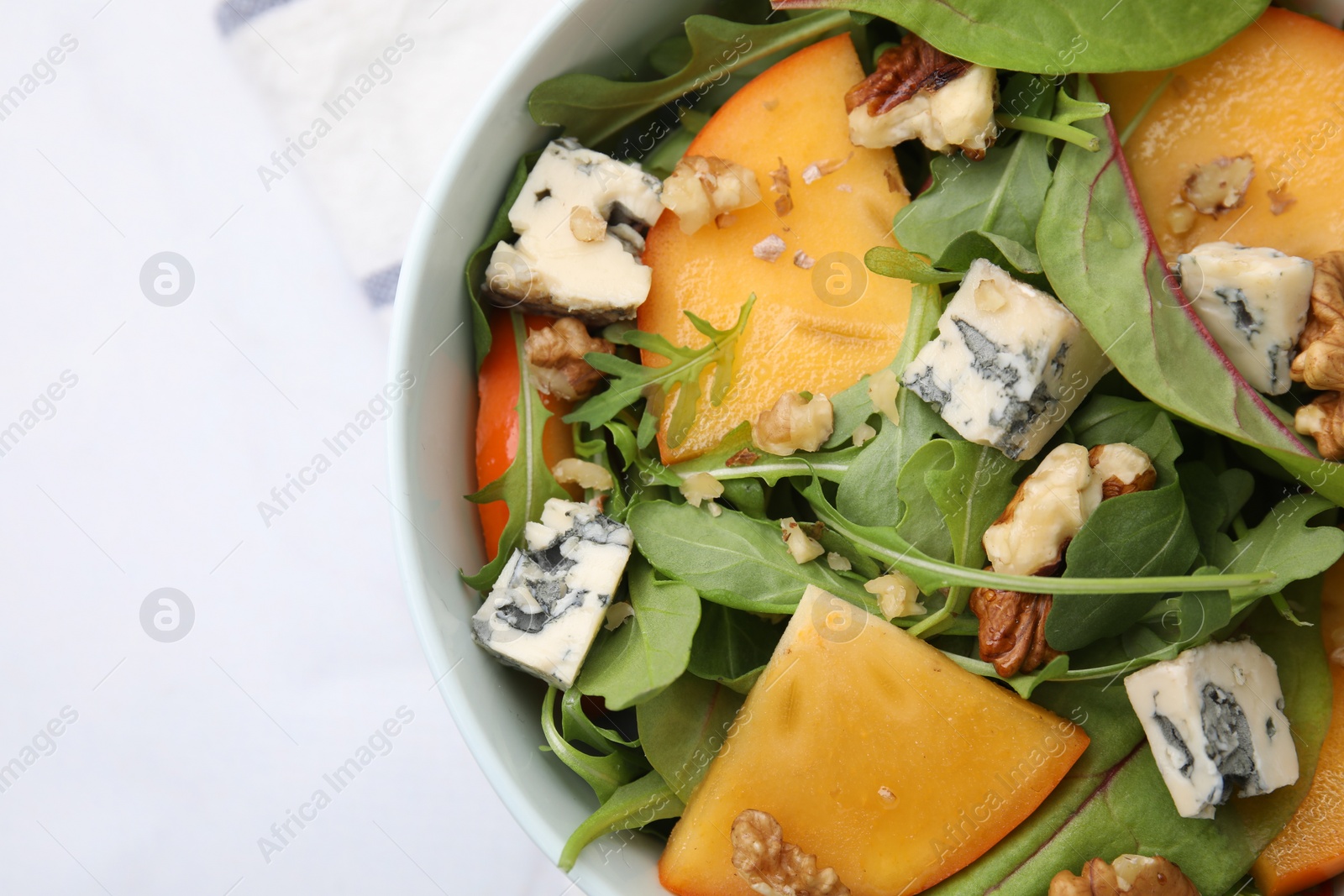 Photo of Tasty salad with persimmon, blue cheese and walnuts served on white table, top view. Space for text