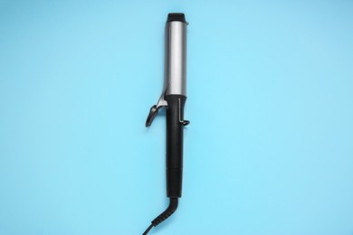 Hair styling appliance. One curling iron on light blue background, top view